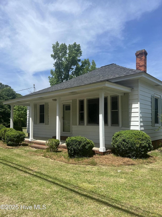 view of front facade featuring a chimney, a front lawn, roof with shingles, and a porch