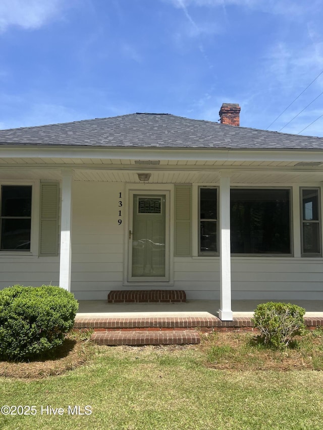 entrance to property featuring a porch, a chimney, and a shingled roof