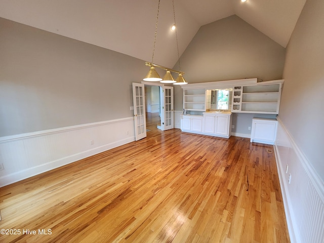 unfurnished dining area with light wood-style floors, a wainscoted wall, and high vaulted ceiling