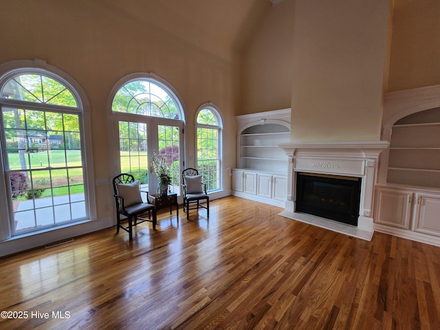 living area featuring a glass covered fireplace, a towering ceiling, visible vents, and a healthy amount of sunlight