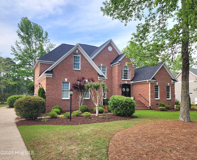 traditional home featuring brick siding, a shingled roof, and a front yard