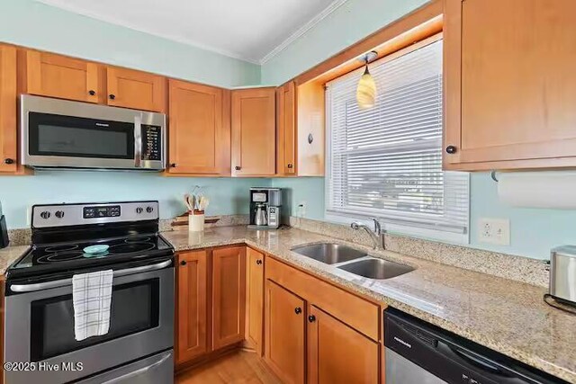 kitchen with crown molding, light stone countertops, brown cabinets, a sink, and stainless steel appliances