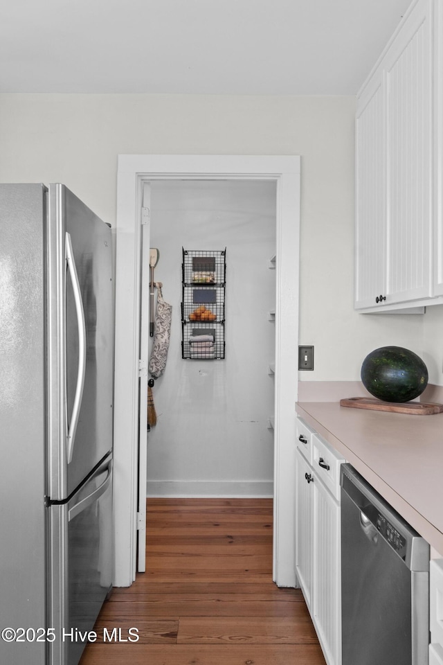 kitchen with white cabinets, appliances with stainless steel finishes, light countertops, baseboards, and wood finished floors