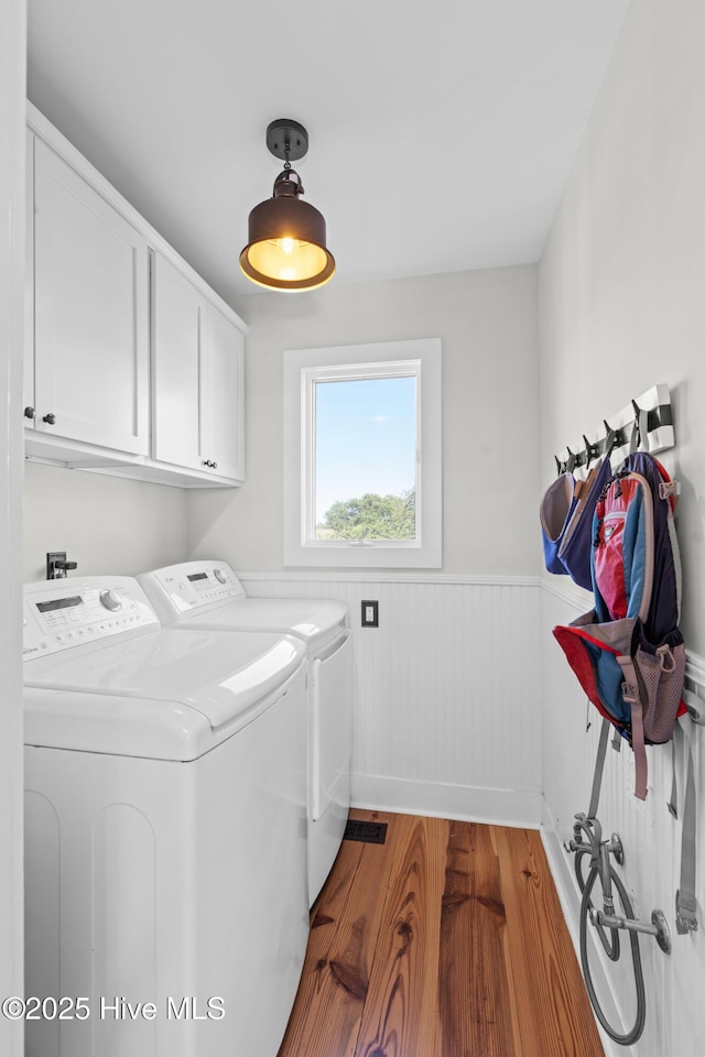 laundry room with cabinet space, independent washer and dryer, wood finished floors, and a wainscoted wall