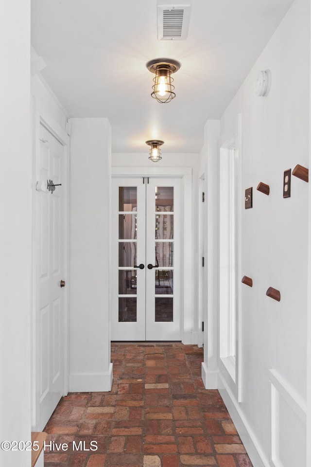 corridor featuring baseboards, visible vents, french doors, and brick floor