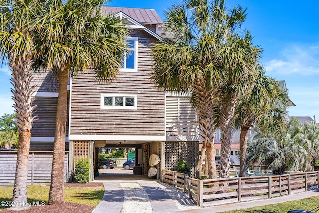 view of front facade featuring concrete driveway, fence, metal roof, and a carport