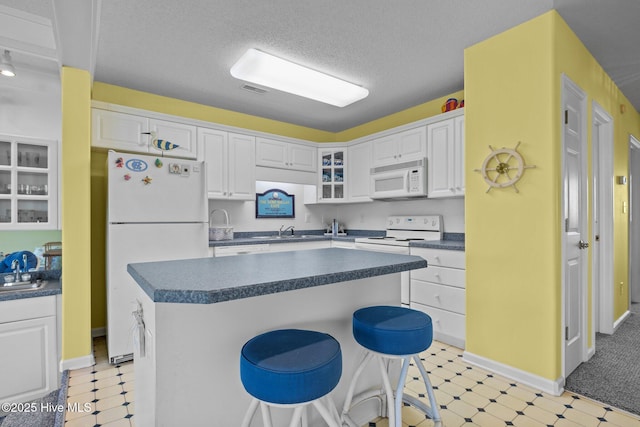 kitchen featuring glass insert cabinets, white cabinetry, white appliances, dark countertops, and light floors