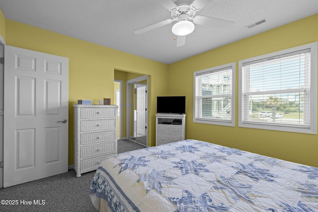bedroom featuring visible vents, dark carpet, a ceiling fan, and a textured ceiling