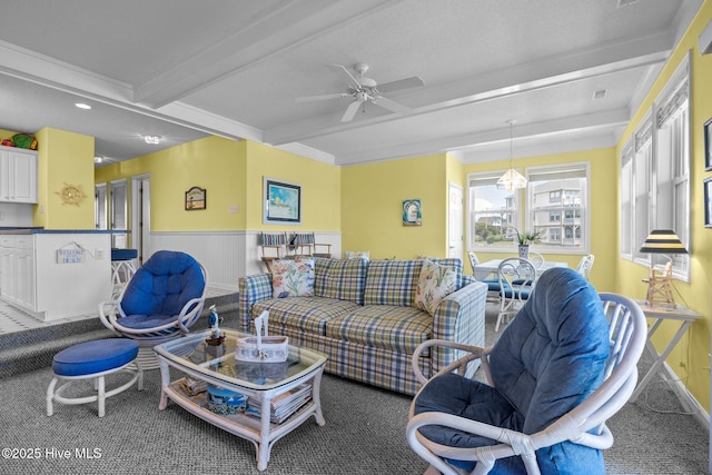 living room featuring beam ceiling, ceiling fan, carpet, baseboards, and wainscoting