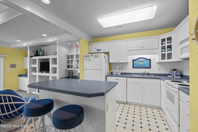 kitchen featuring a sink, a kitchen bar, white appliances, dark countertops, and white cabinets