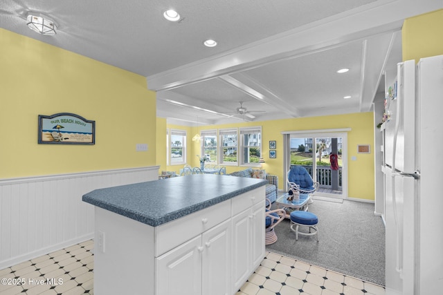 kitchen with light floors, dark countertops, beamed ceiling, and wainscoting