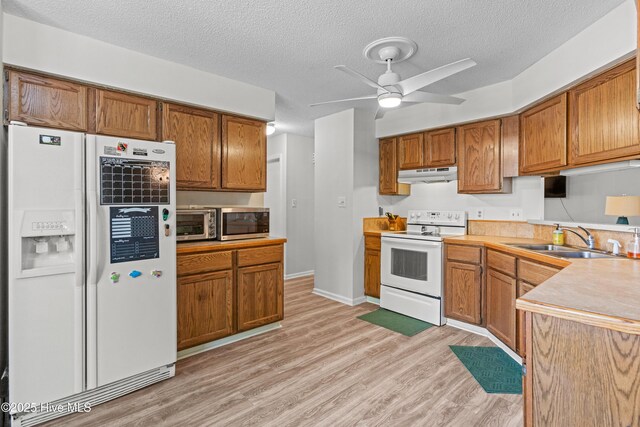 kitchen with a sink, under cabinet range hood, light wood finished floors, white appliances, and a ceiling fan