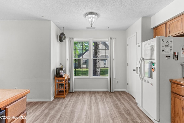 interior space with a textured ceiling, white refrigerator with ice dispenser, visible vents, light wood-type flooring, and brown cabinetry