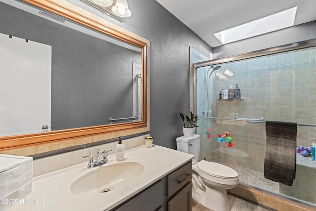bathroom with a shower stall, vanity, toilet, a textured wall, and a skylight