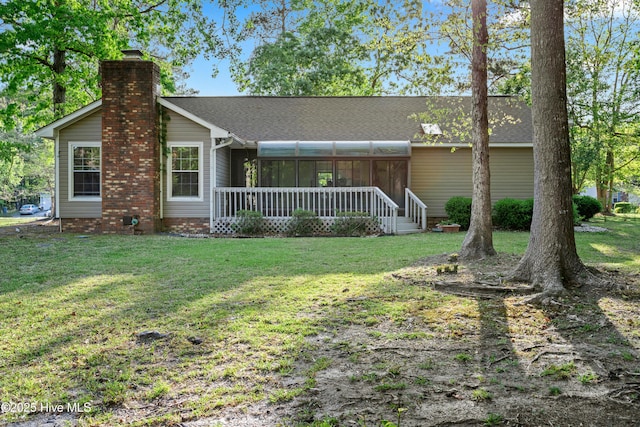 view of front of property with a chimney, a shingled roof, a front lawn, and a sunroom