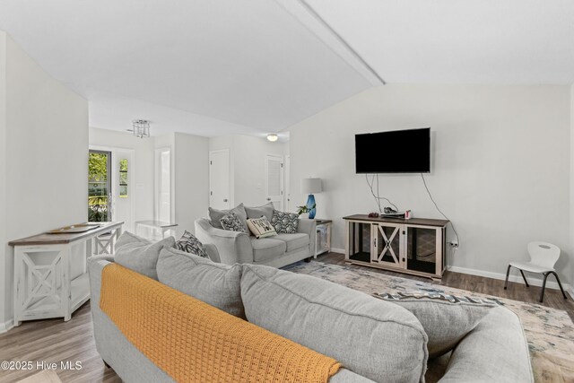 living area with wood finished floors, vaulted ceiling, and baseboards