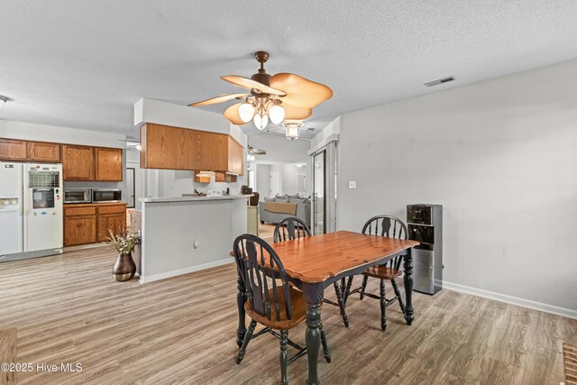 dining room featuring a textured ceiling, ceiling fan, light wood-type flooring, and baseboards
