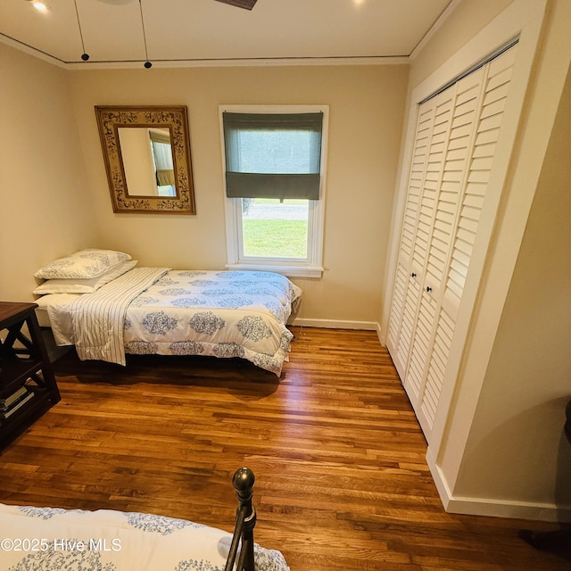 bedroom with baseboards, ornamental molding, dark wood-type flooring, and a closet
