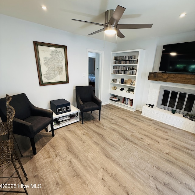 sitting room with a ceiling fan, wood finished floors, built in features, baseboards, and a brick fireplace