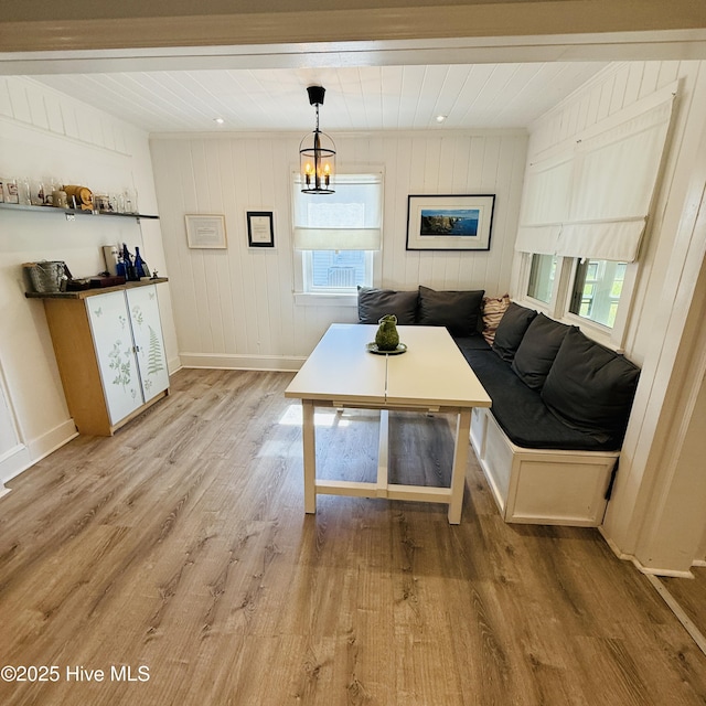 living room featuring a notable chandelier, wood walls, a healthy amount of sunlight, and light wood-style flooring