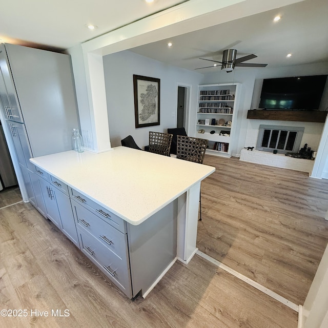 kitchen with ceiling fan, a peninsula, light wood finished floors, and light countertops