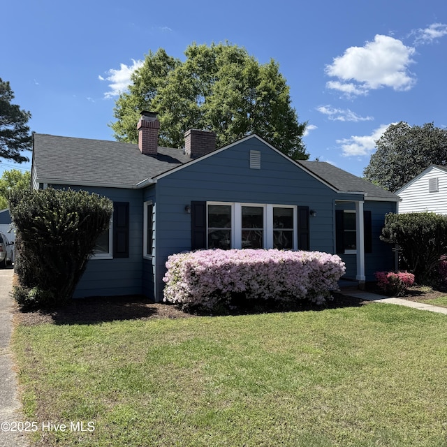 bungalow-style house featuring a front lawn, a shingled roof, and a chimney