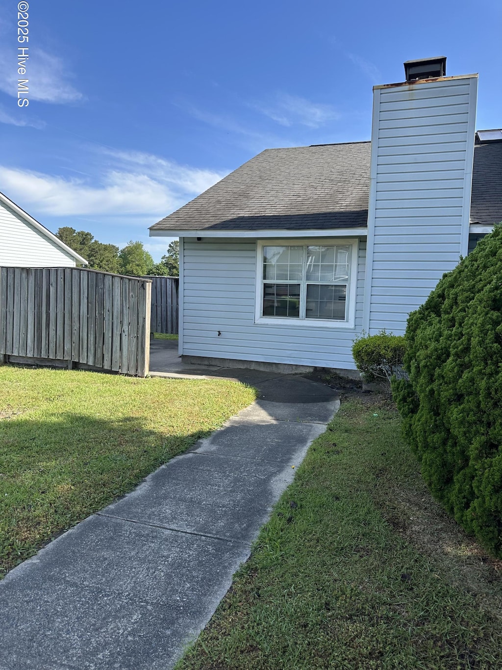 view of side of property featuring a lawn, fence, a chimney, and a shingled roof
