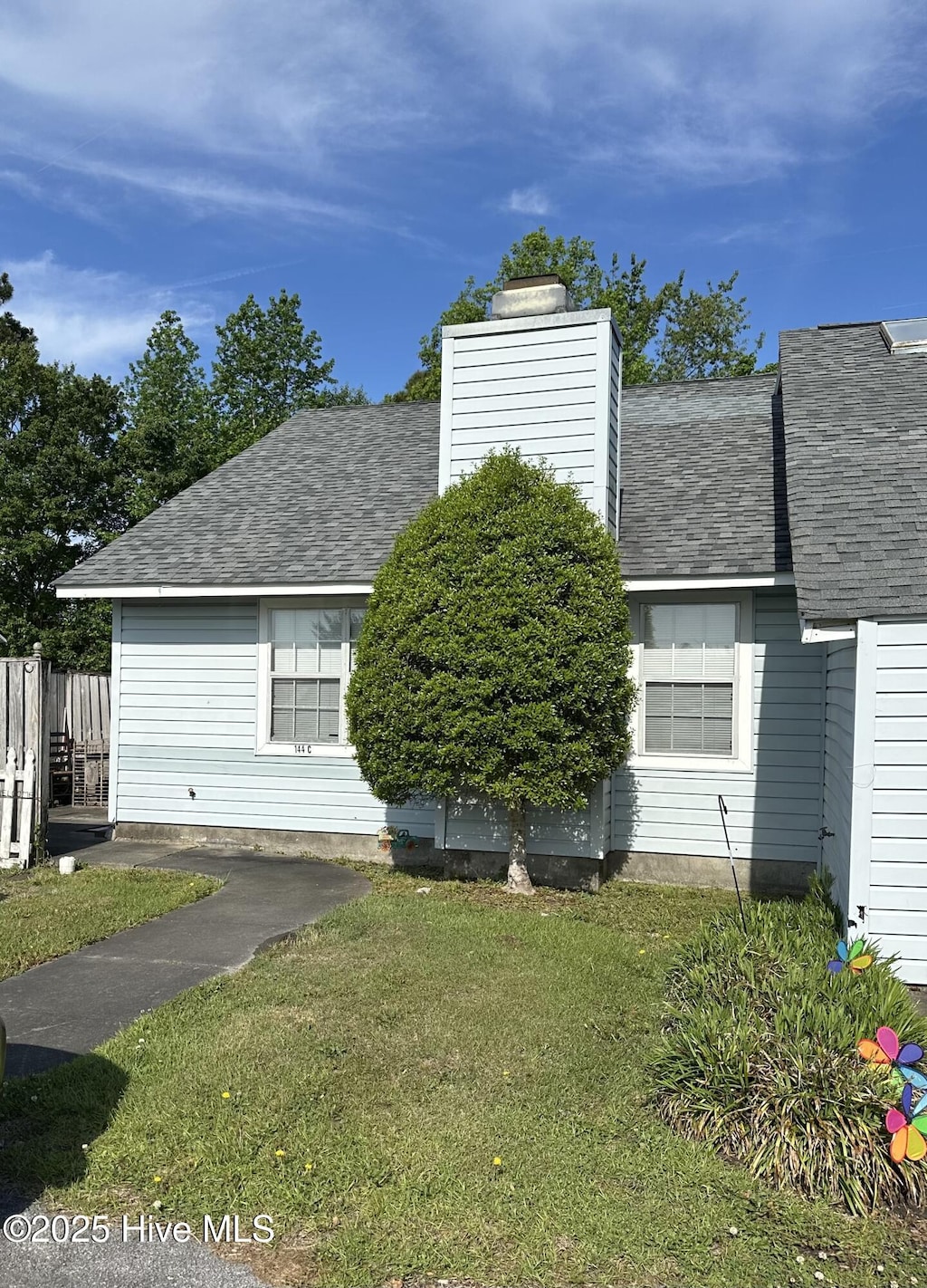 view of front facade featuring fence, roof with shingles, a chimney, and a front lawn