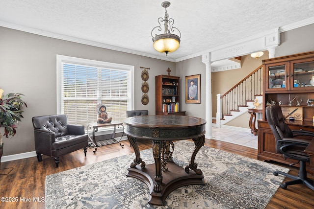 office space featuring ornamental molding, a textured ceiling, wood finished floors, and ornate columns