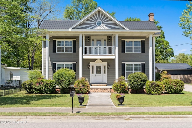 greek revival inspired property with a chimney, fence, a front yard, and metal roof