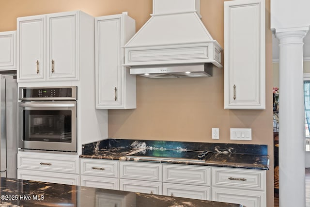 kitchen with dark stone counters, custom range hood, white cabinets, and stainless steel appliances