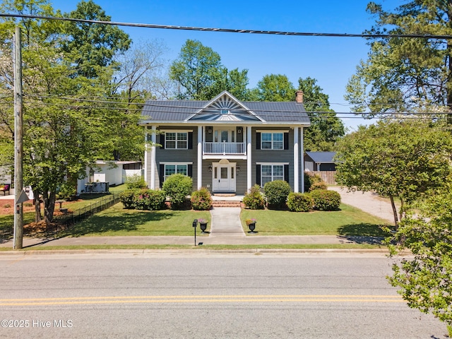 view of front of house with a balcony, a chimney, metal roof, a standing seam roof, and a front yard
