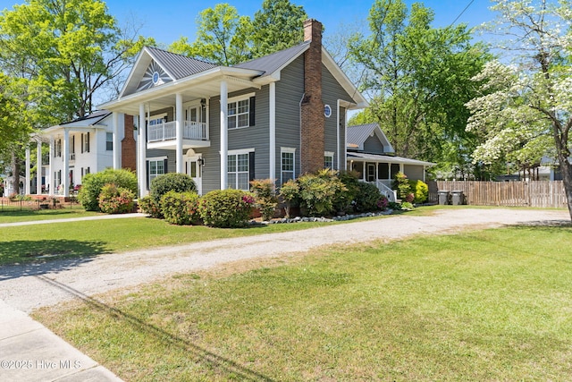 view of front facade with a chimney, fence, dirt driveway, a balcony, and a front yard
