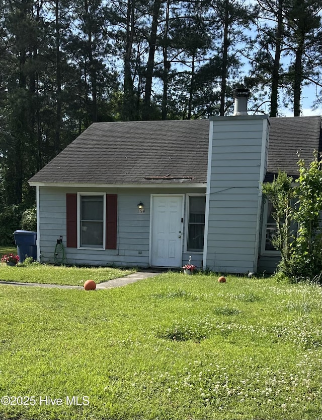 view of front of house featuring roof with shingles, a chimney, and a front lawn