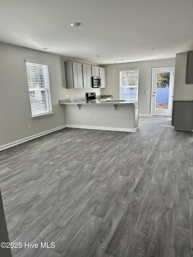 kitchen featuring light stone counters, appliances with stainless steel finishes, baseboards, a kitchen breakfast bar, and dark wood-type flooring