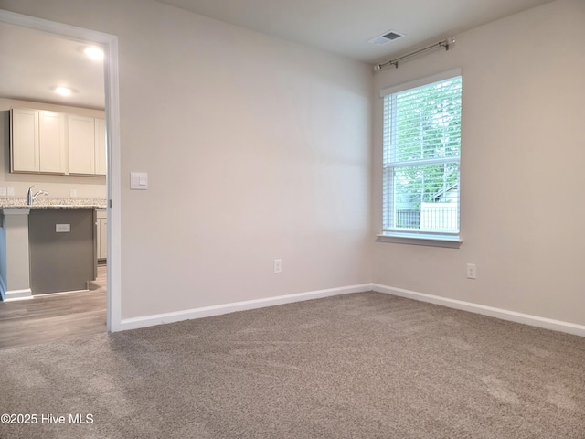 unfurnished room featuring a sink, visible vents, baseboards, and light carpet
