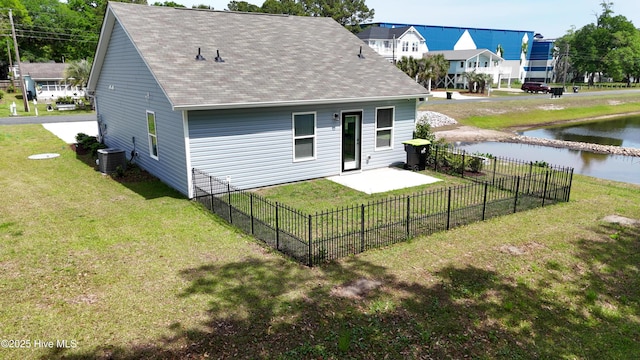 rear view of property featuring a water view, a shingled roof, central air condition unit, a yard, and fence private yard