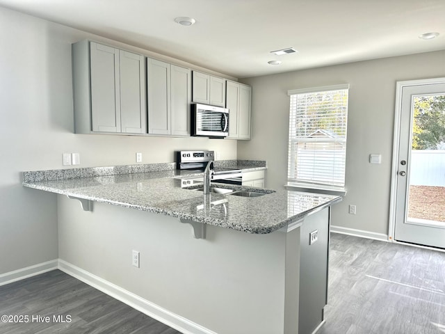 kitchen with a breakfast bar area, gray cabinets, stainless steel appliances, and light wood-style floors
