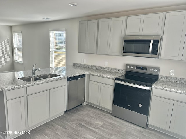 kitchen featuring light stone counters, stainless steel appliances, a peninsula, and a sink