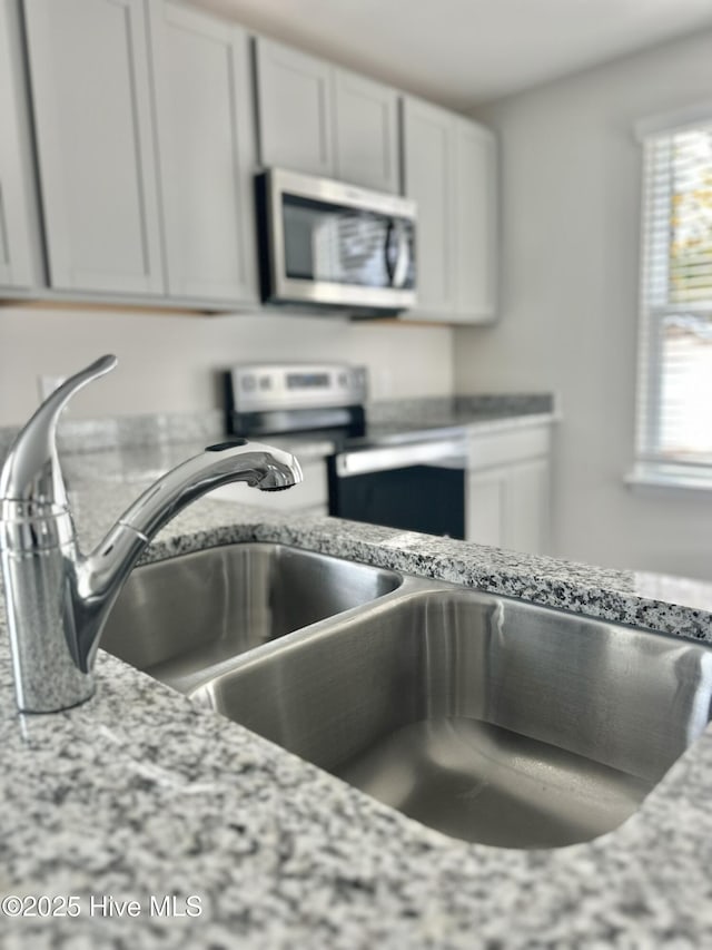 kitchen with white cabinetry, light stone countertops, stainless steel appliances, and a sink