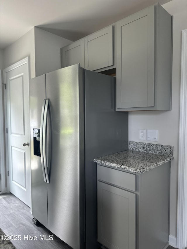 kitchen with gray cabinetry, light stone countertops, stainless steel fridge, and light wood-style flooring