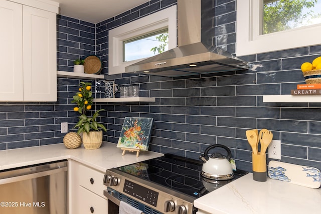 kitchen with wall chimney range hood, white cabinetry, tasteful backsplash, open shelves, and appliances with stainless steel finishes