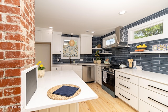 kitchen with a sink, stainless steel appliances, open shelves, light wood-type flooring, and wall chimney exhaust hood