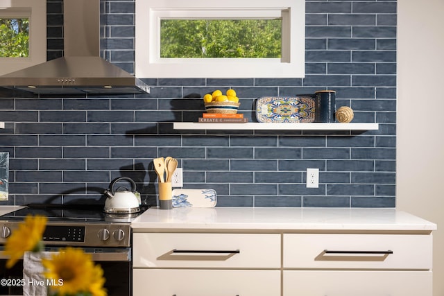 room details featuring wall chimney exhaust hood, backsplash, stainless steel electric range oven, and white cabinetry