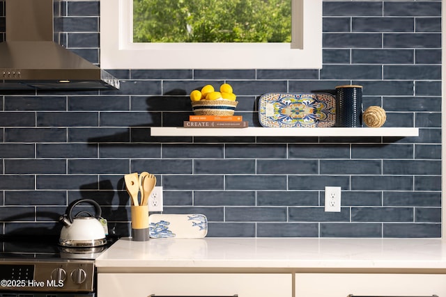 interior details with white cabinetry, backsplash, and wall chimney exhaust hood