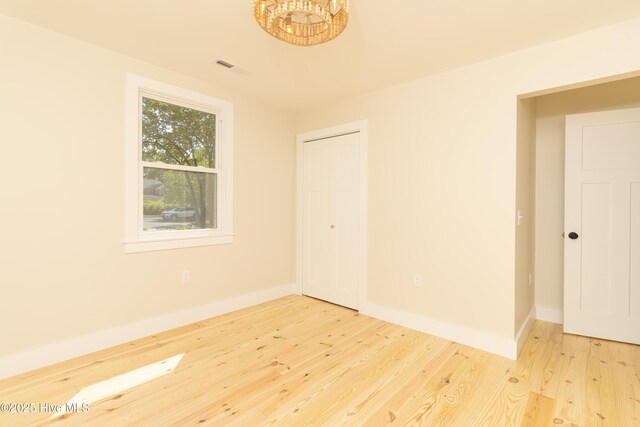 spare room with an inviting chandelier, wood finished floors, visible vents, and baseboards