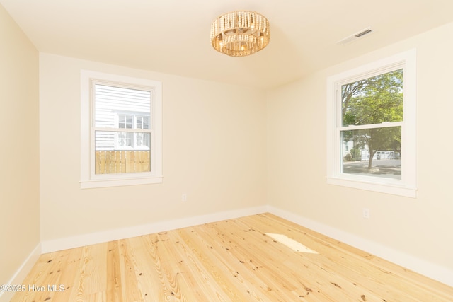 spare room featuring a chandelier, wood finished floors, visible vents, and baseboards
