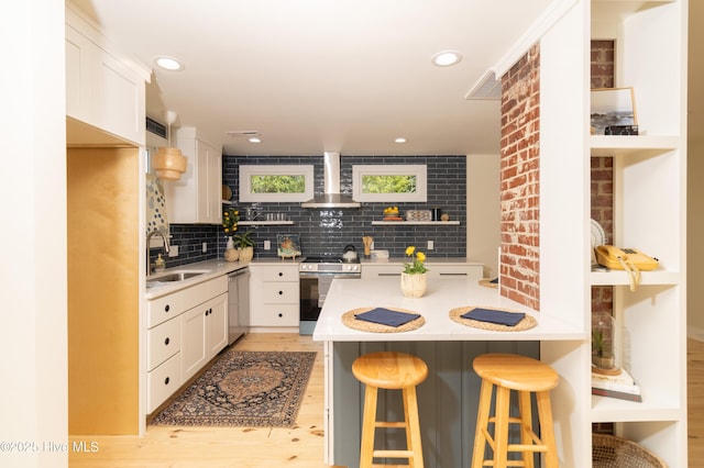 kitchen featuring a sink, stainless steel appliances, open shelves, wall chimney range hood, and light countertops