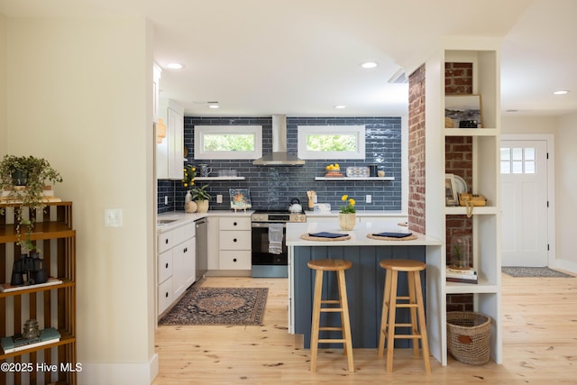 kitchen with stainless steel appliances, open shelves, wall chimney range hood, white cabinets, and light wood finished floors