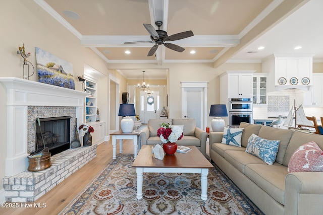 living room with crown molding, light wood-type flooring, ceiling fan, a fireplace with raised hearth, and a chandelier